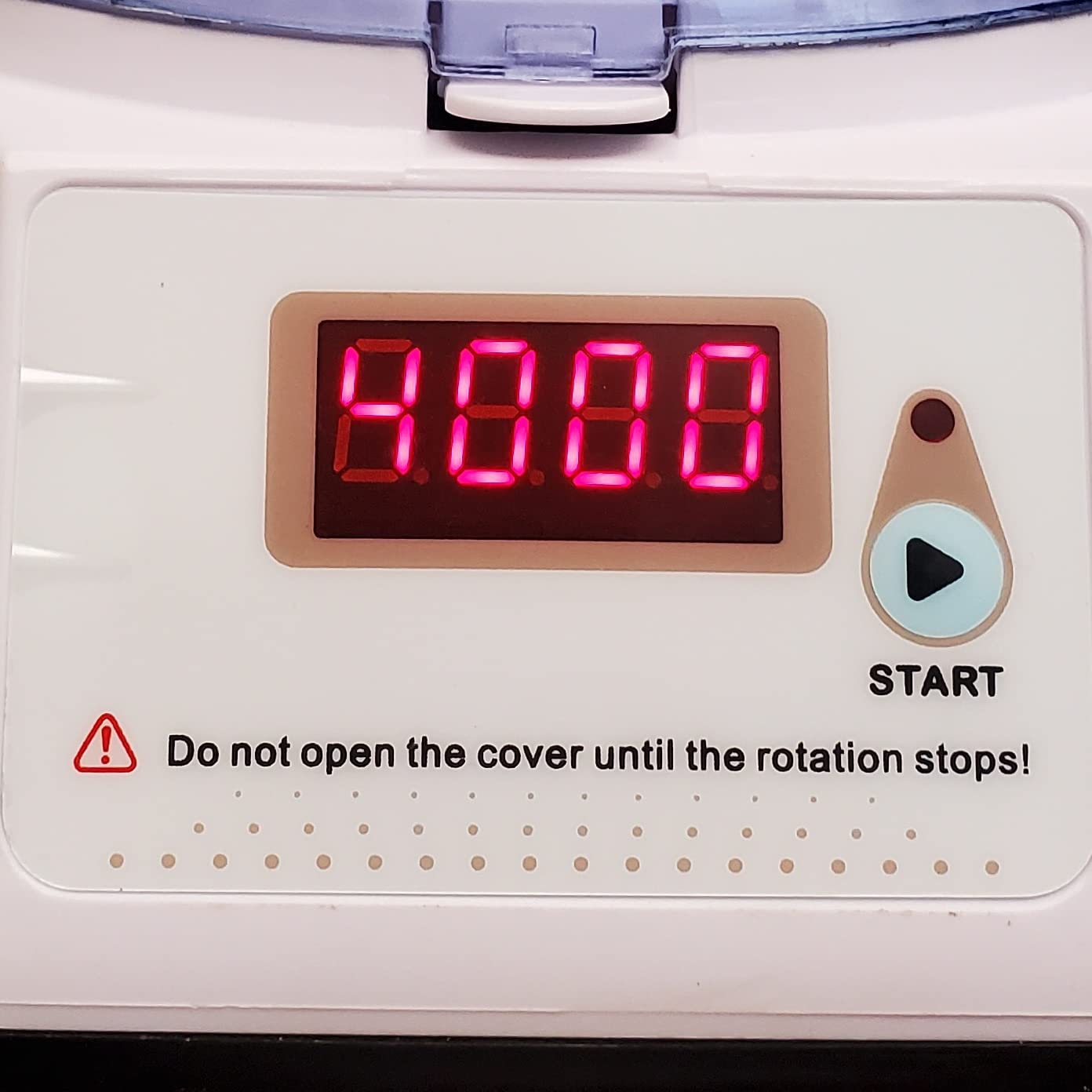 Close-up of the digital display and control panel of a Labnique mini centrifuge. The display shows "8888" in red digits. To the right is a "START" button with a play symbol. Below the display is a warning triangle and text that reads "Do not open the cover until the rotation stops!" The panel also has a row of small dots along the bottom edge.