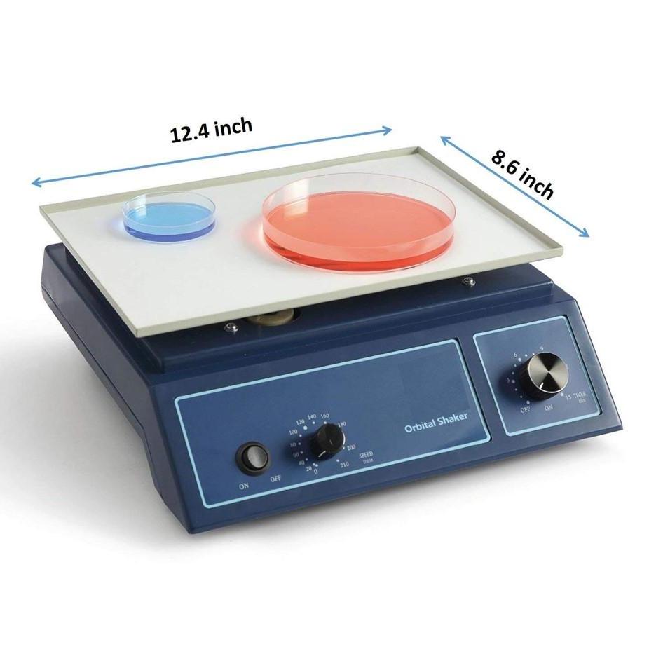 An orbital shaker with a blue base and a white platform. Two petri dishes, one blue and one red, are on the platform. The dimensions of the platform are labeled as 12.4 inches and 8.6 inches.