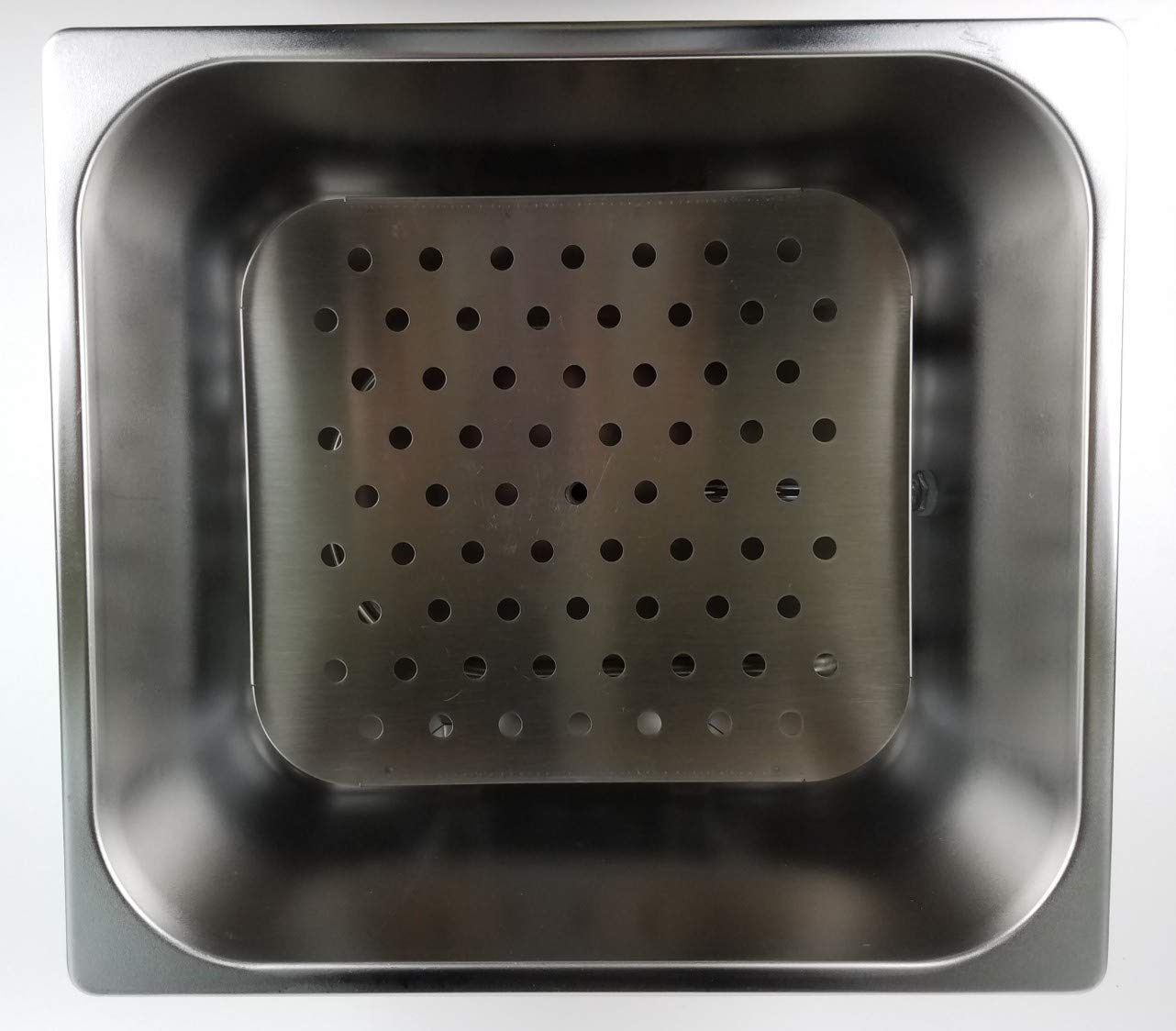 Overhead view of a stainless steel water bath interior with a perforated, removable false bottom.