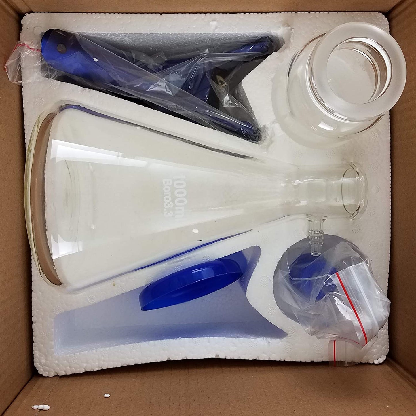 Glass vacuum filtration apparatus components, including a 1000ml flask, securely packed in foam within a cardboard box.