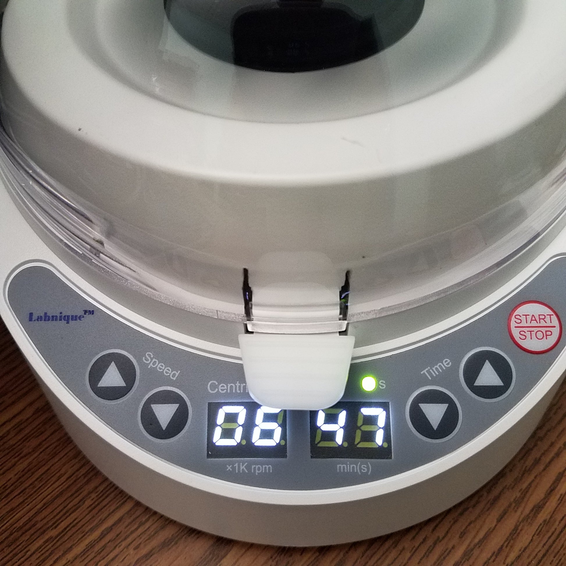 A white Labnique mini centrifuge with a clear dome-shaped lid that is open. The centrifuge has a black rotor inside with several holes for tubes. The control panel on the front has several buttons and a digital display showing "88 88". The centrifuge is shown against a white background.